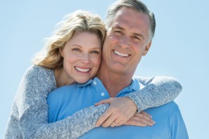 Portrait of loving mature woman embracing man from behind against clear blue sky