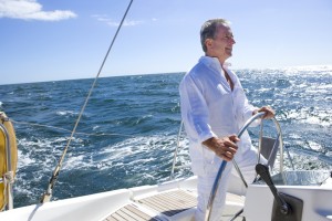 Mature man standing at helm of yacht out at sea, steering, smiling, side view (tilt)