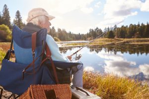 Senior man sits fishing in a lake, back view close-up